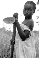 A young African girl wielding a metal hoe.